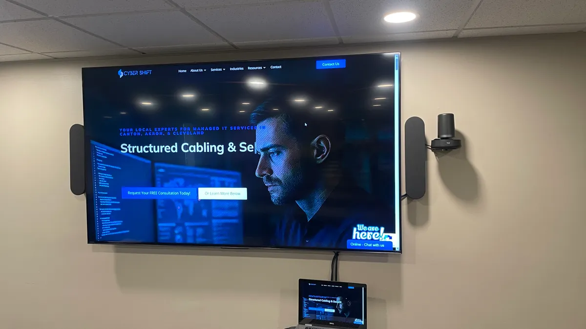 A meeting-room display with a mounted conference camera and speakers showing the Cyber Shift website