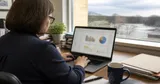 An office manager at a desk reviewing a color-coded spreadsheet on a monitor in a small Northeast Ohio office