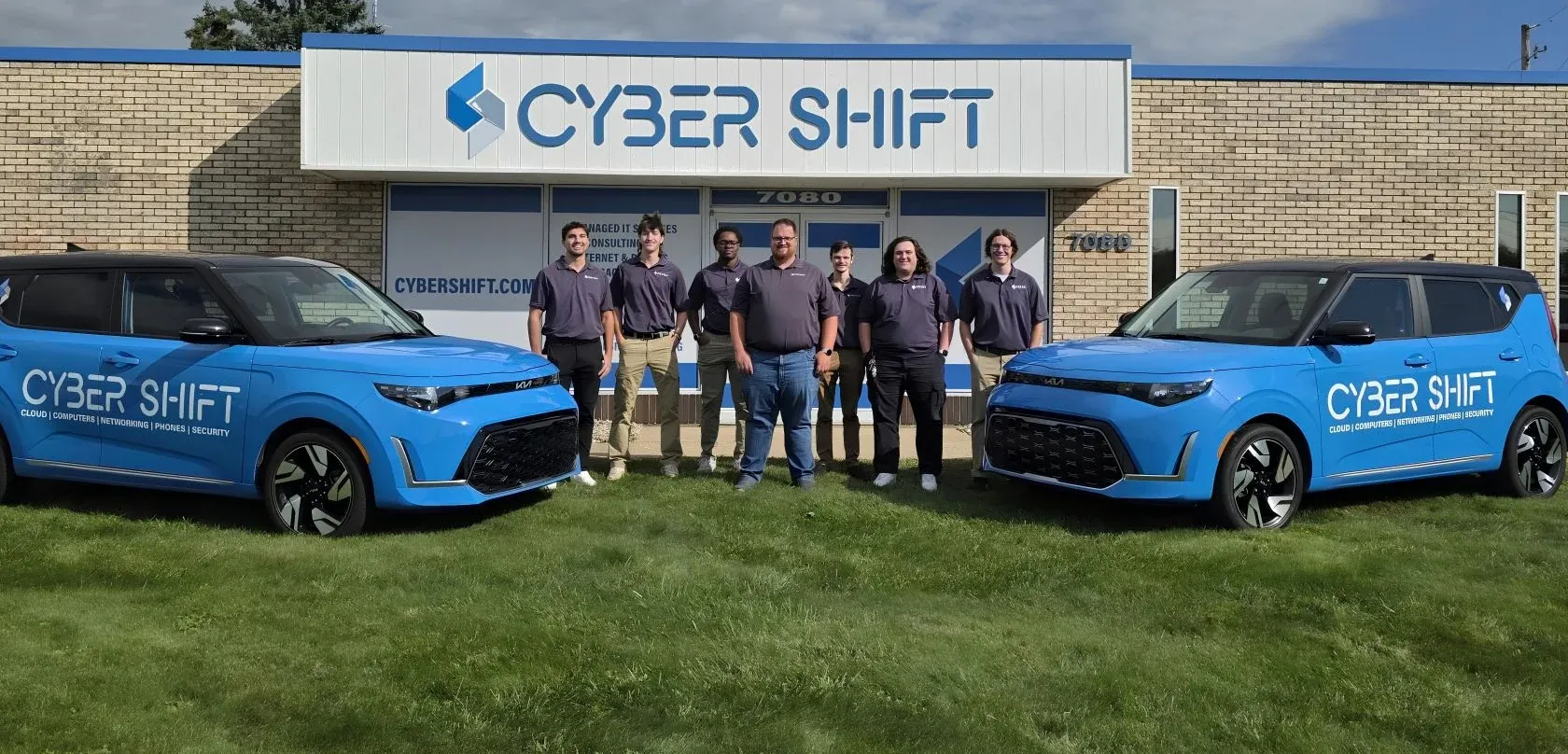 Seven members of the Cyber Shift team standing between two branded vehicles outside the North Canton office.