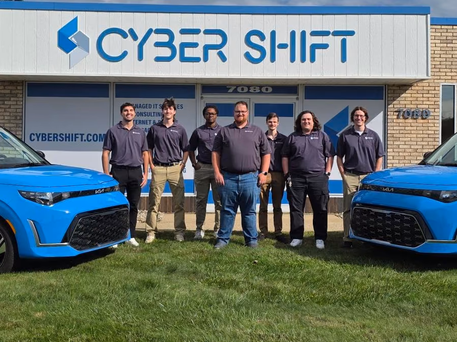 The Cyber Shift team standing outside the North Canton office between two blue Cyber Shift vehicles.